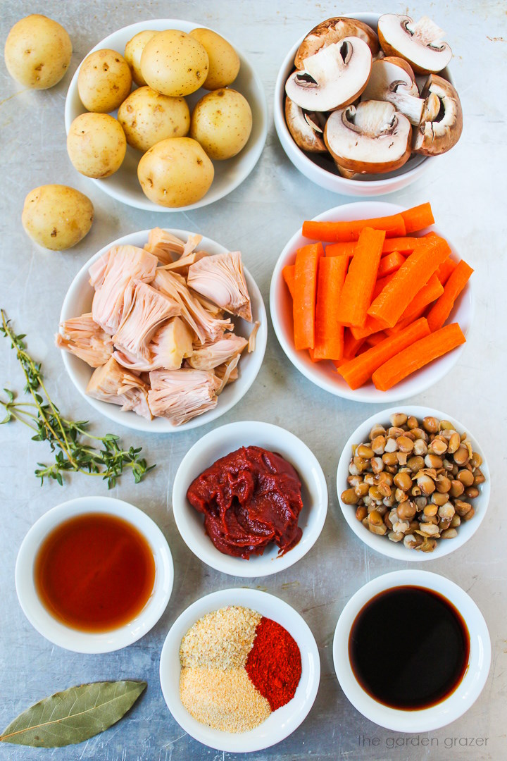 Baby potatoes, mushrooms, lentils, carrots, jackfruit, tomato paste, and seasoning ingredients laid out on a metal tray