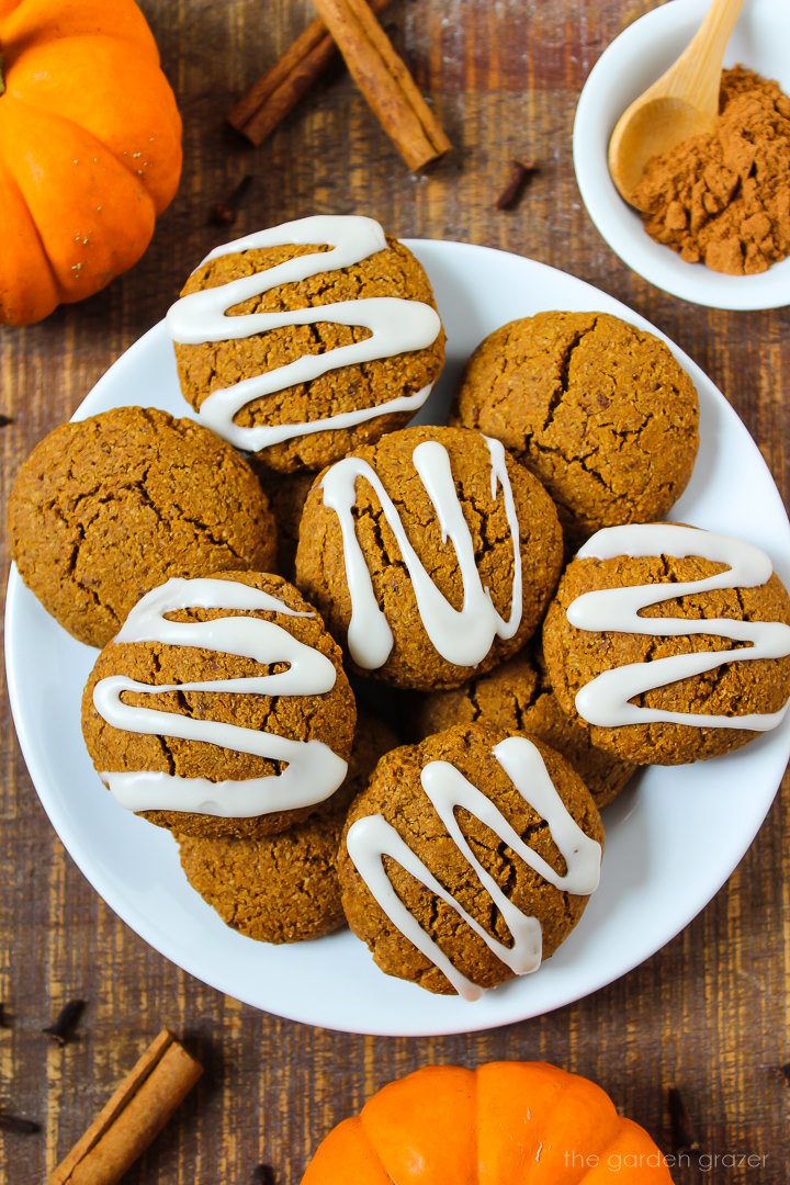 Vegan pumpkin cookies with sugar icing on a white serving plate on a wooden table