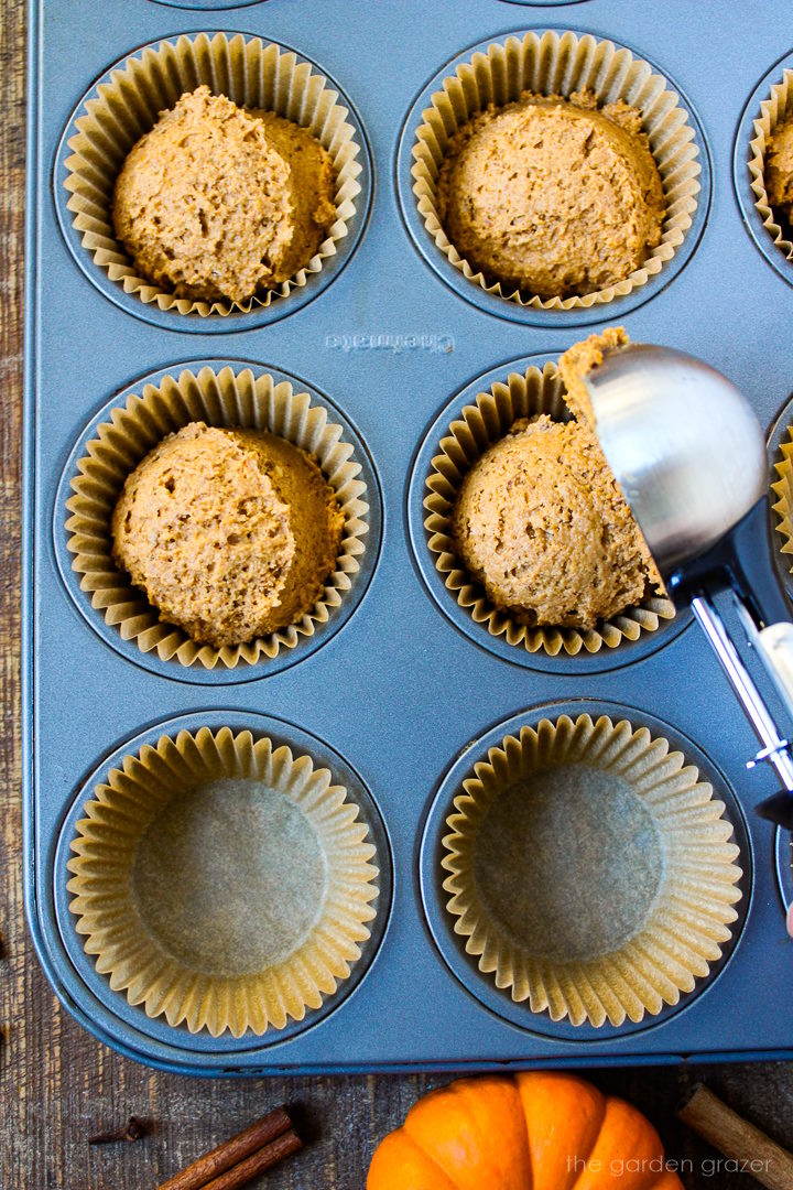 Scooping vegan pumpkin muffins batter into baking cups with a metal scoop