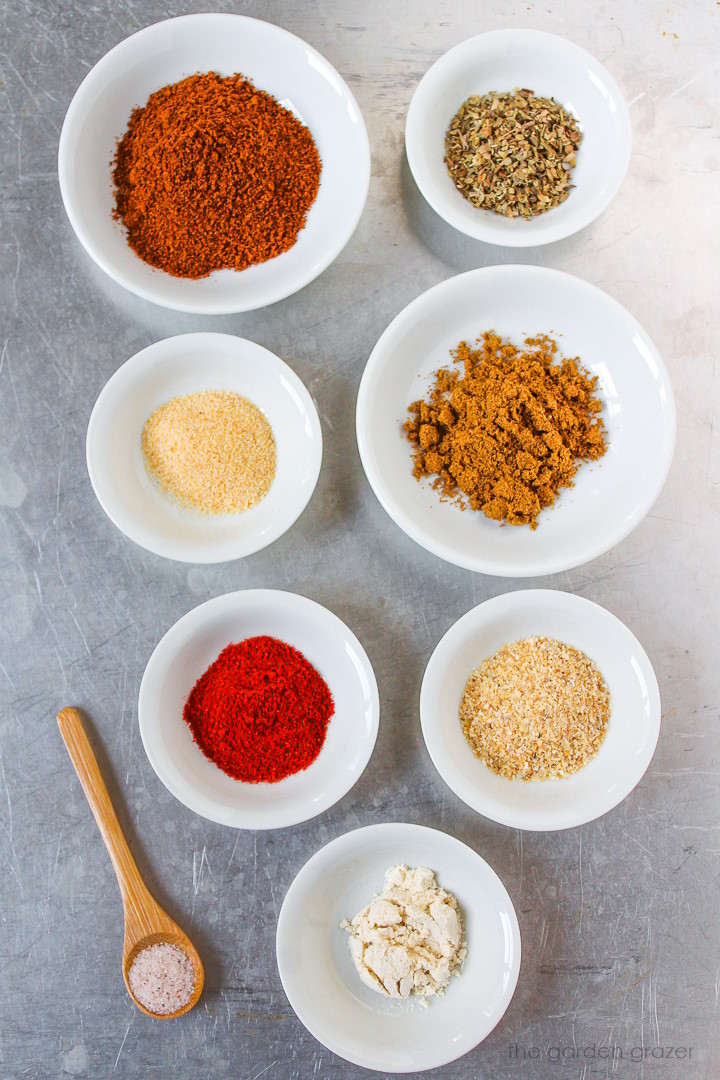 Various spice ingredients laid out in white bowls on a metal tray