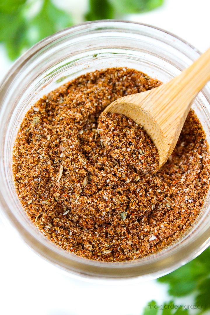 Overhead view of chili seasoning recipe mixed together in a small glass jar with wooden spoon