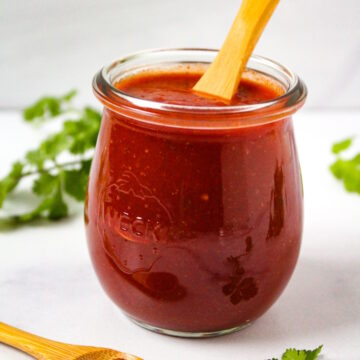 Homemade red taco sauce in a small glass jar with serving spoon