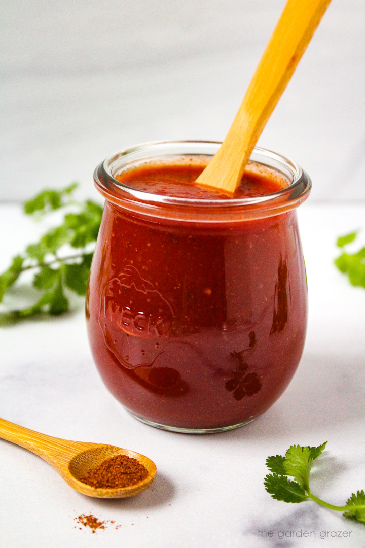 Homemade red taco sauce in a small glass jar with serving spoon