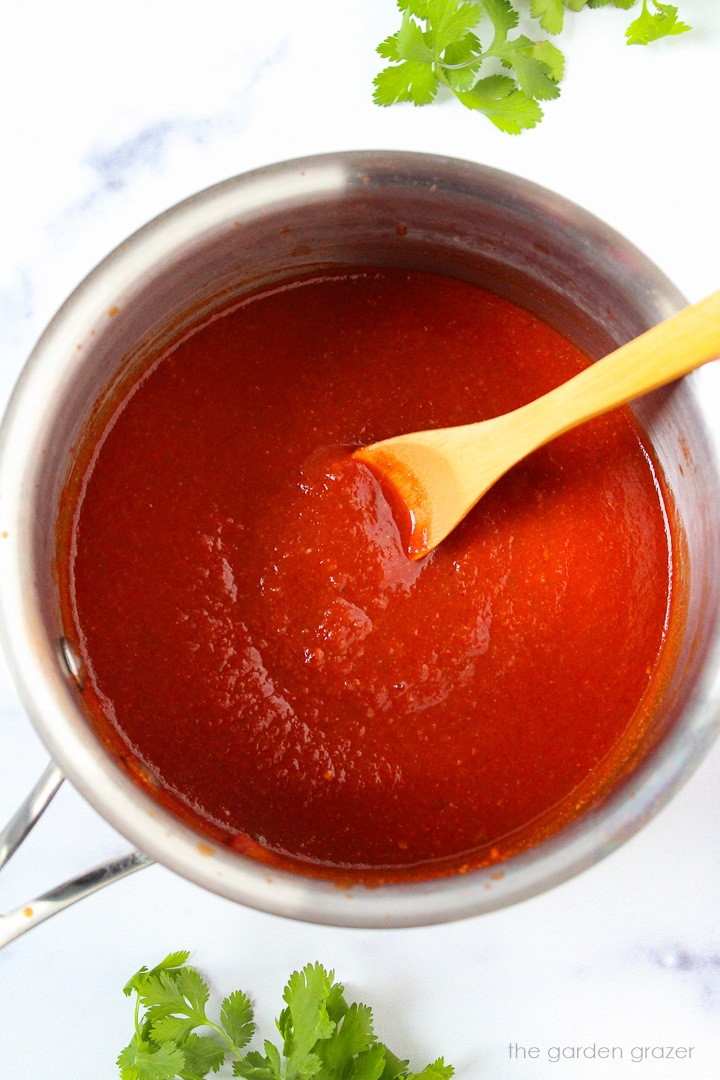 Overhead view of taco sauce recipe cooking in a small saucepan with wooden stirring spoon