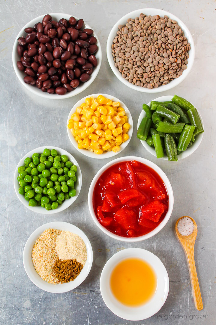 Black beans, lentils, diced tomatoes, sweet corn, peas, green beans, and spice ingredients laid out on a metal tray