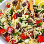 Greek orzo pasta salad in a white serving bowl with wooden spoons