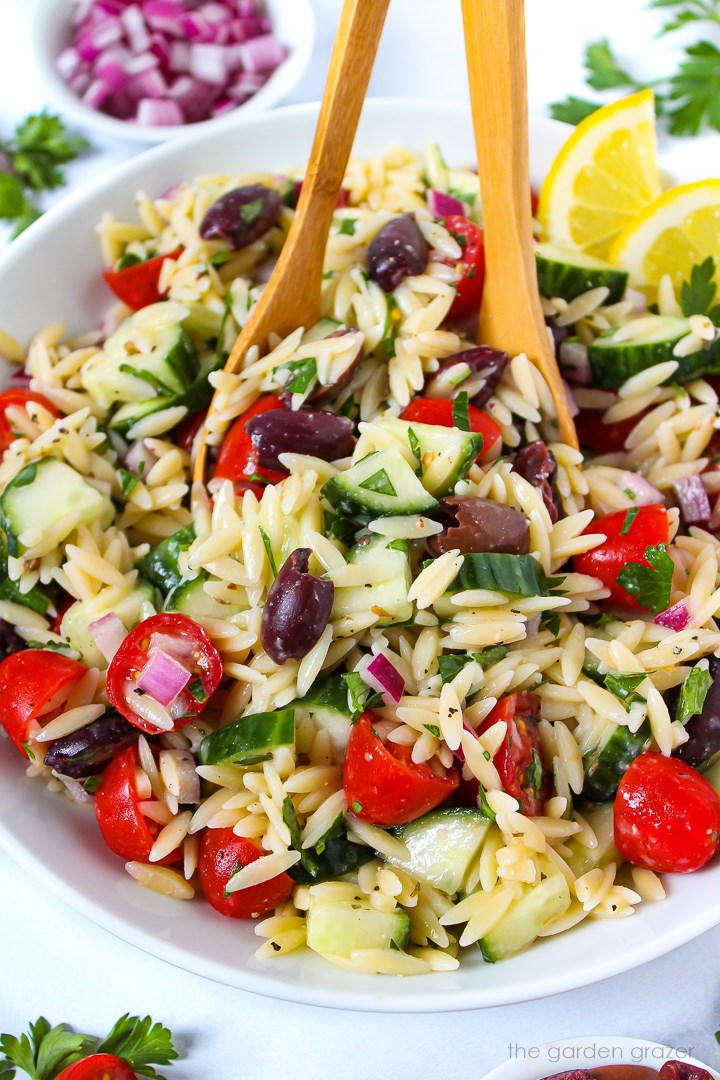 Greek orzo pasta salad in a white serving bowl with wooden spoons