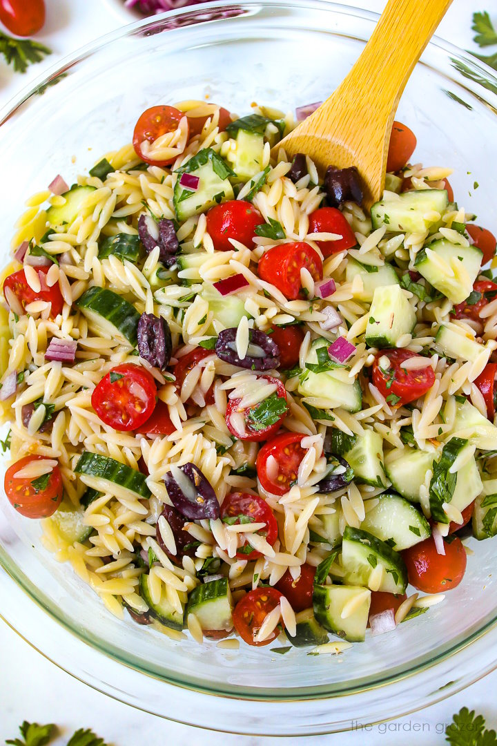 Greek orzo pasta salad in a large mixing bowl with wooden spoon