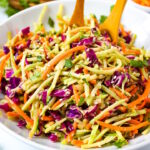 Asian broccoli slaw with sesame ginger dressing in a white serving bowl with wooden spoons