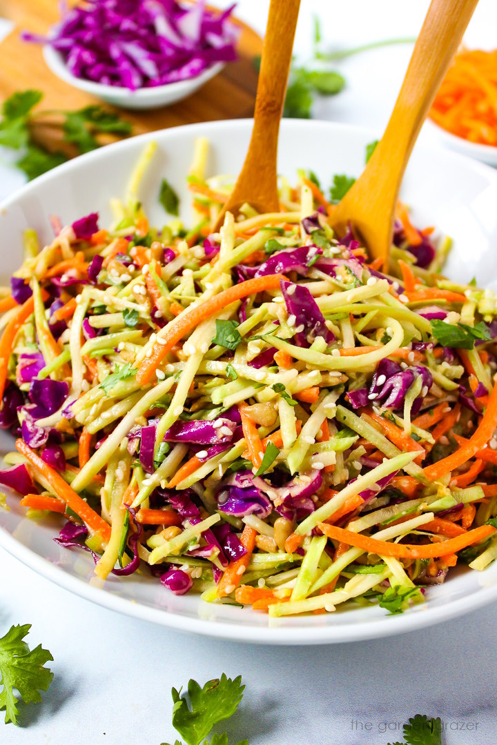 Asian broccoli slaw with sesame ginger dressing in a white serving bowl with wooden spoons