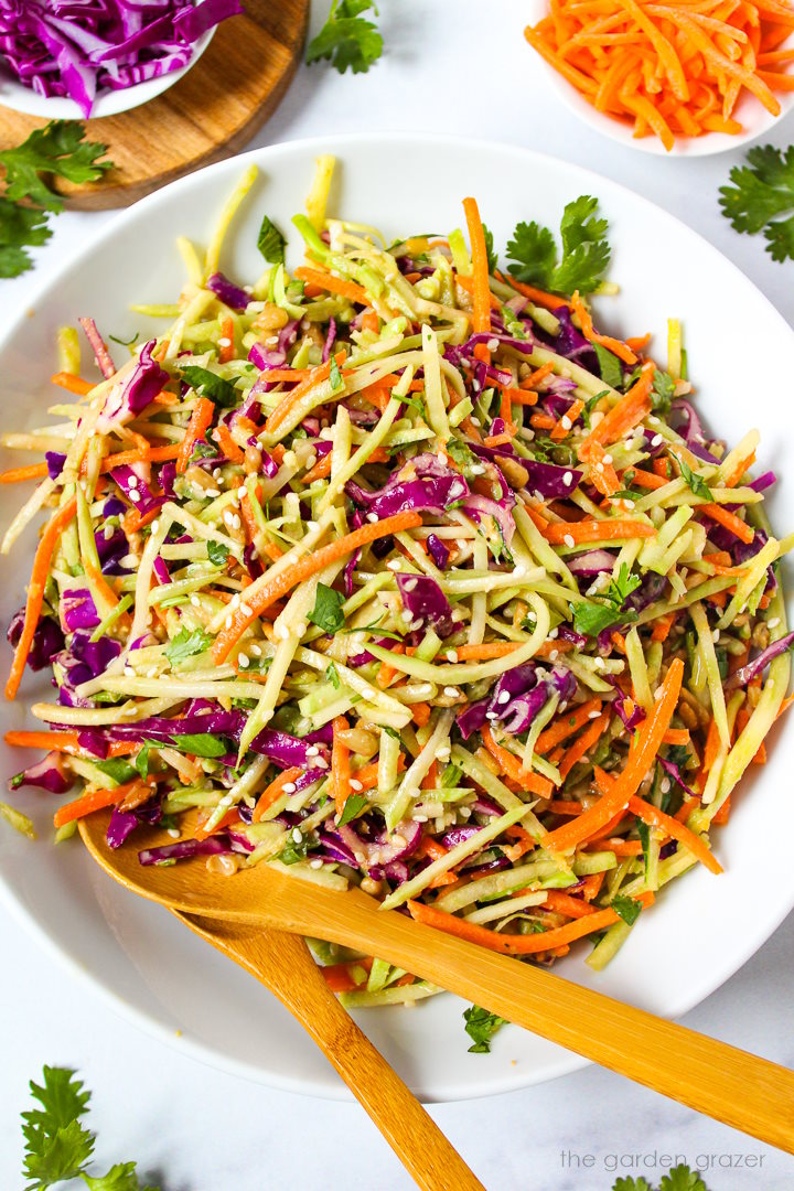 Overhead view of Asian broccoli slaw with sesame ginger dressing in a white bowl with serving spoons