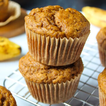 Two gluten-free vegan banana muffins stacked on a cooling rack after baking