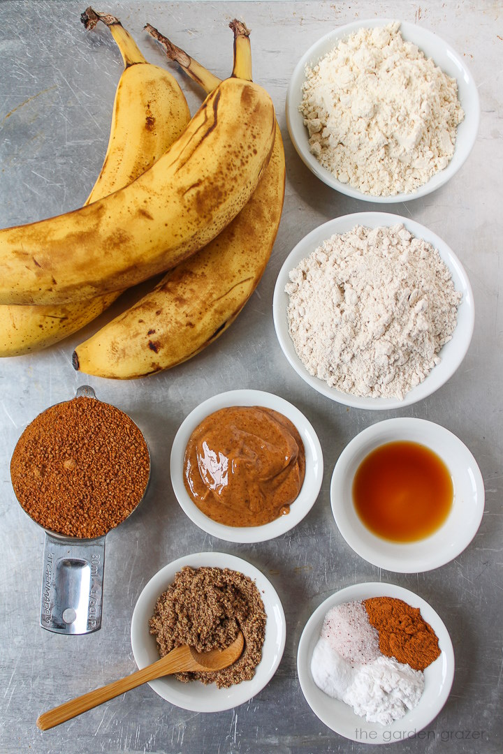 Ripe bananas, flour, coconut sugar, almond butter, vanilla extract, and flax ingredients laid out on a metal tray