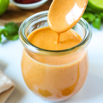 A wooden spoon lifting up creamy chipotle lime dressing from a small glass jar