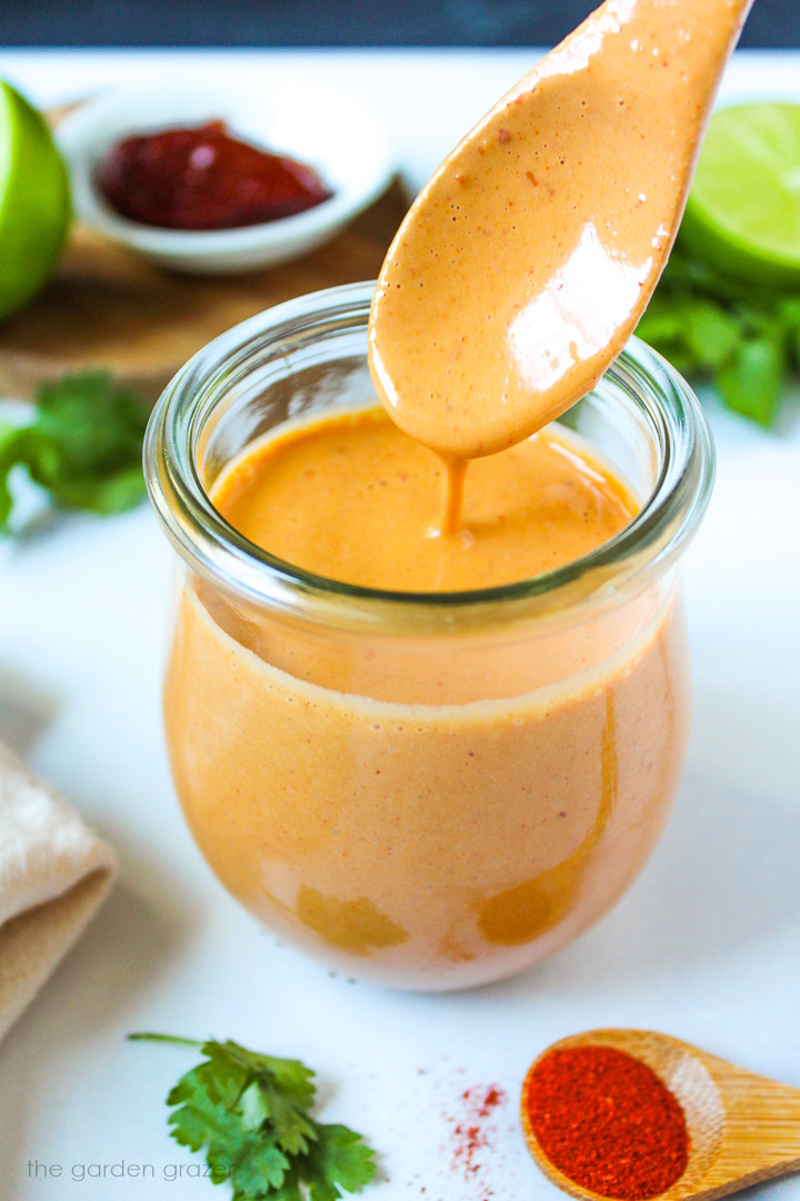 A wooden spoon lifting up creamy chipotle lime dressing from a small glass jar