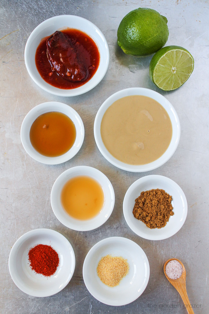 Tahini, fresh limes, maple syrup, peppers in adobo, vinegar, and spice ingredients laid out on a metal tray