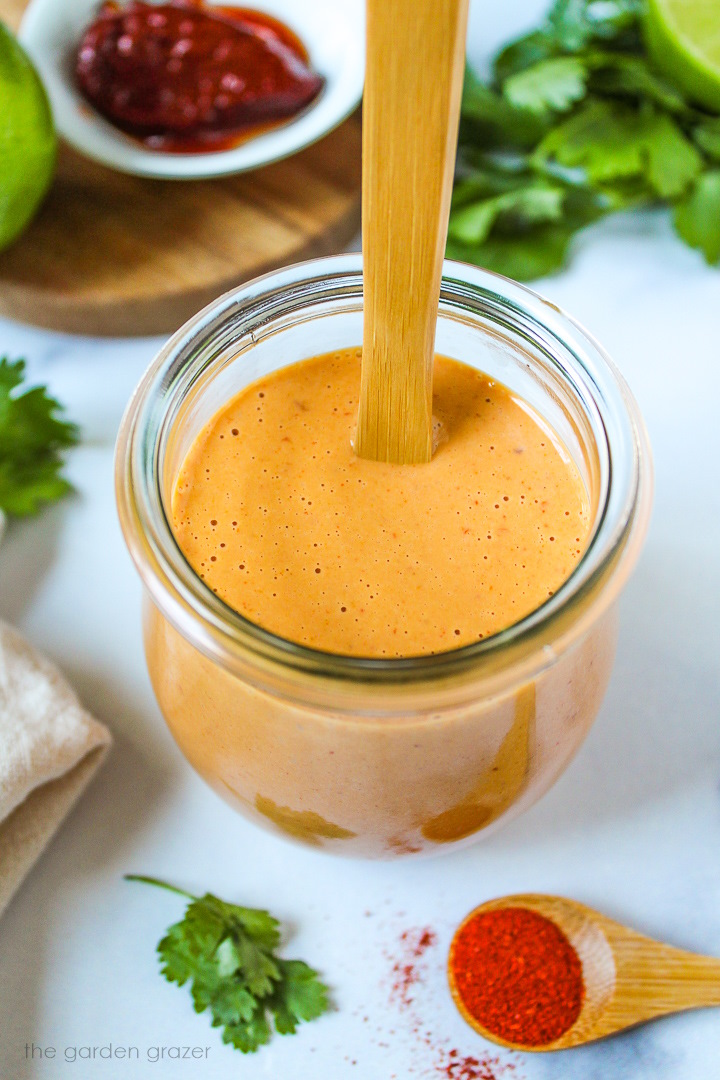 Overhead view of vegan creamy chipotle lime dressing in a small jar with serving spoon