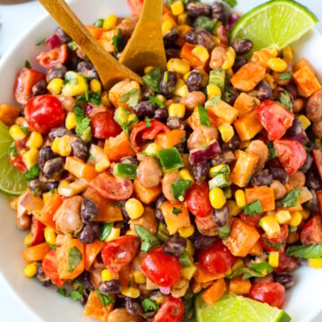 Mexican bean salad with creamy chipotle dressing in a white serving bowl with wooden spoons