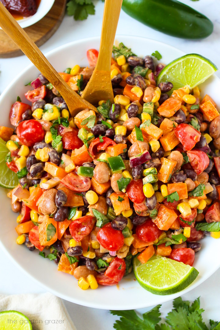 Mexican bean salad with creamy chipotle dressing in a white serving bowl with wooden spoons