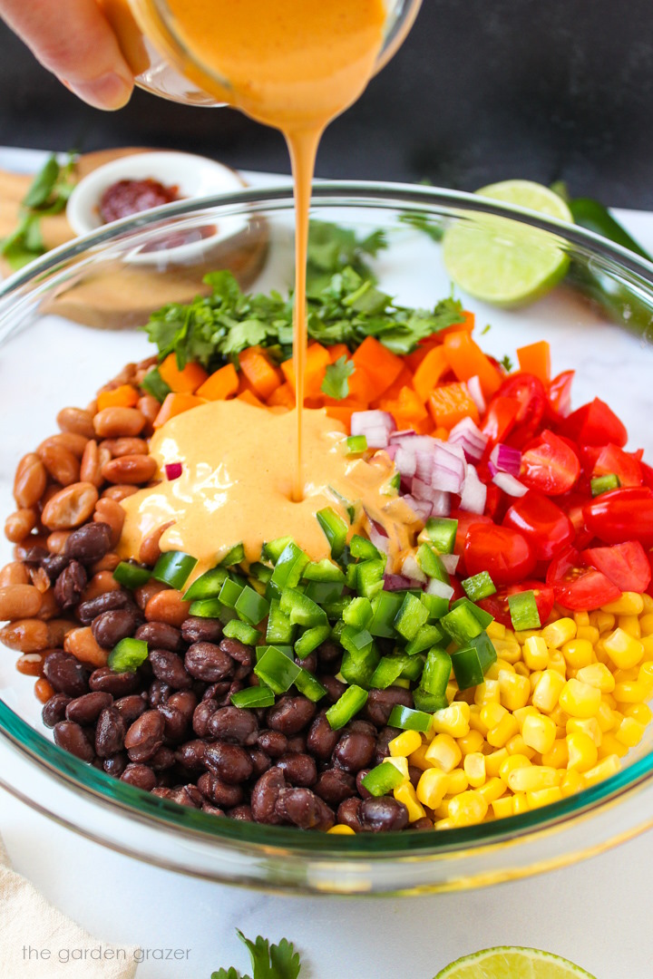 Creamy chipotle lime dressing being poured over Mexican bean salad ingredients in a large mixing bowl