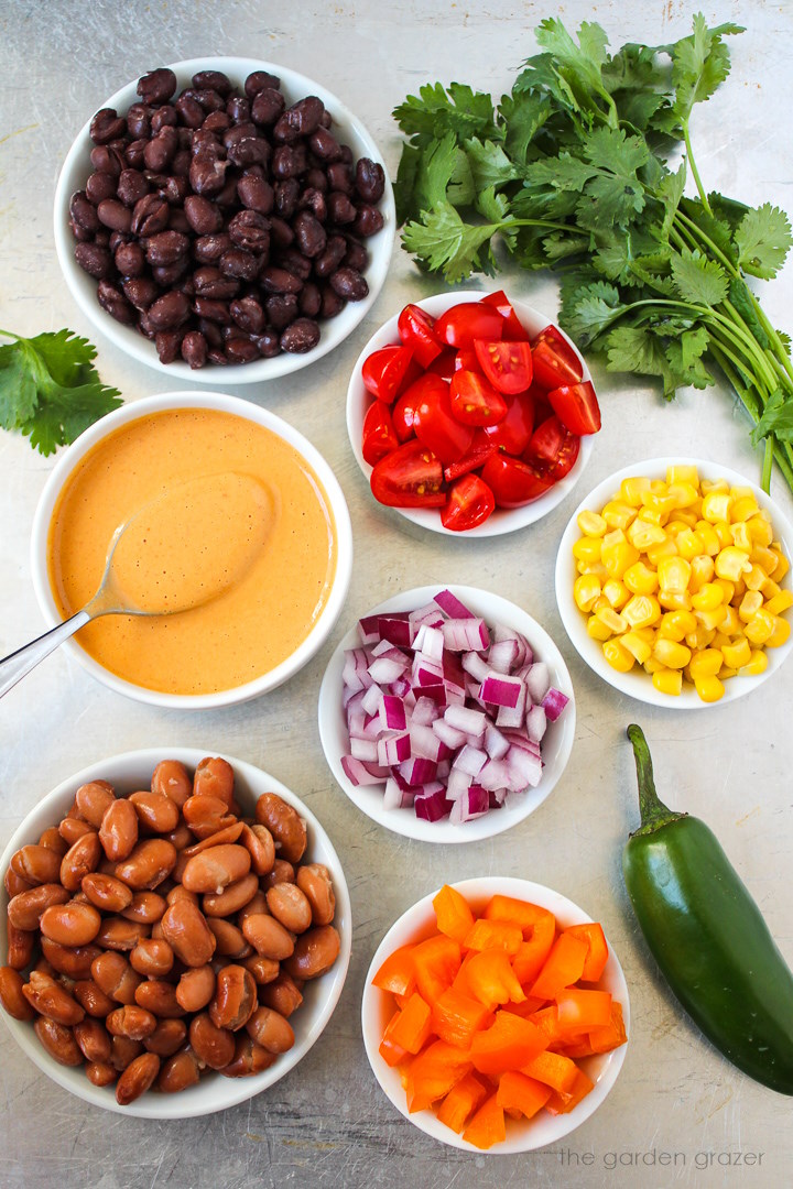 Black beans, pinto beans, sweet corn, tomatoes, onion, cilantro, and dressing ingredients laid out on a metal tray