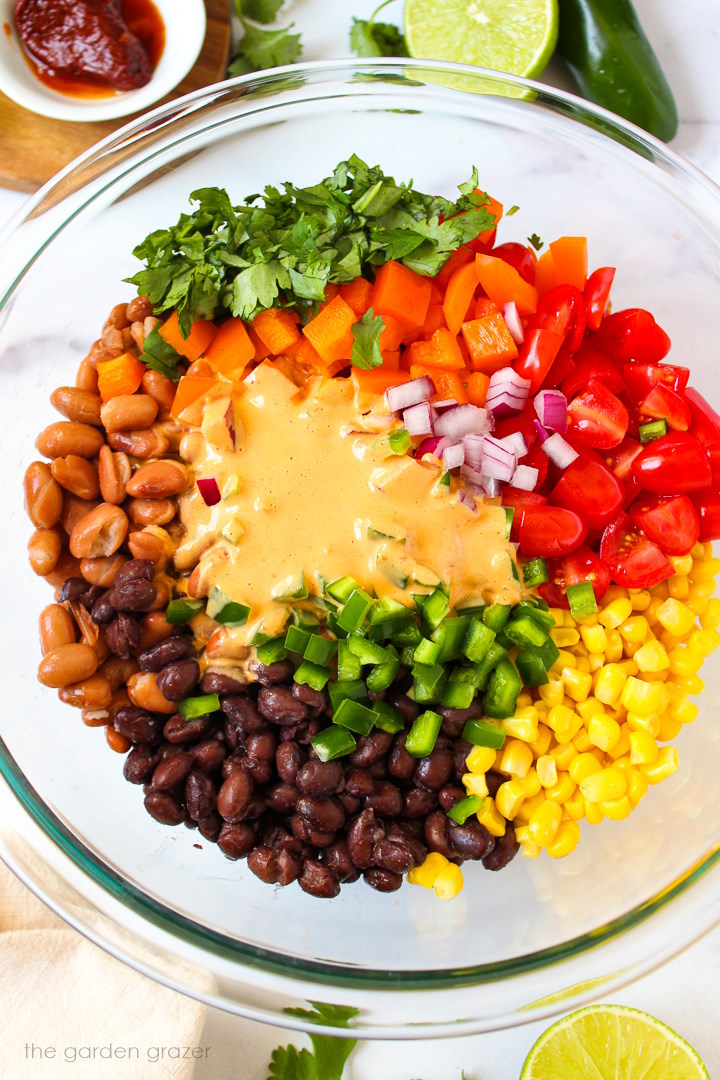 Overhead view of preparing Mexican bean salad in a large glass bowl before mixing together